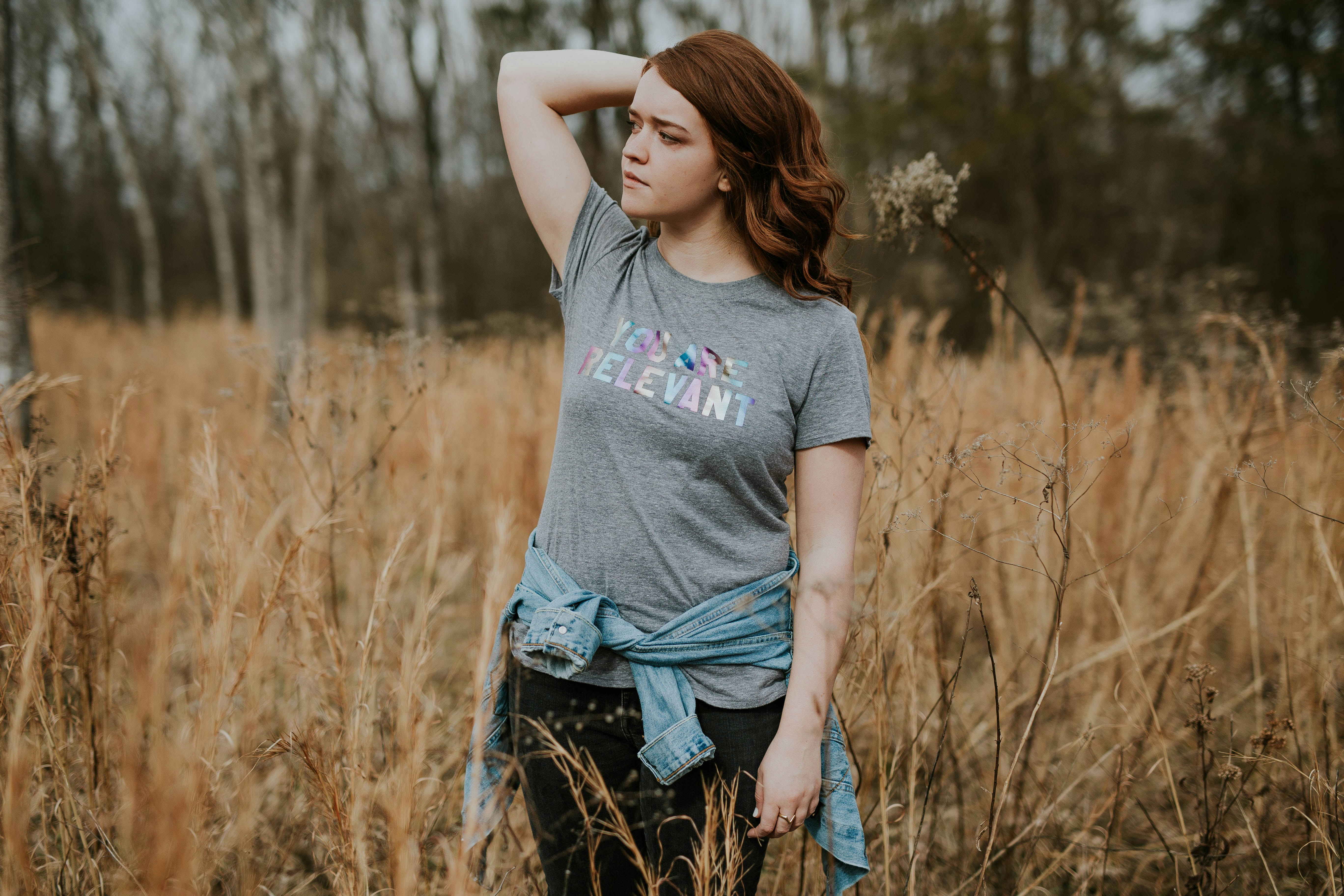 shallow focus photography of woman in gray crew-neck shirt standing in the middle of brown grass field during daytime